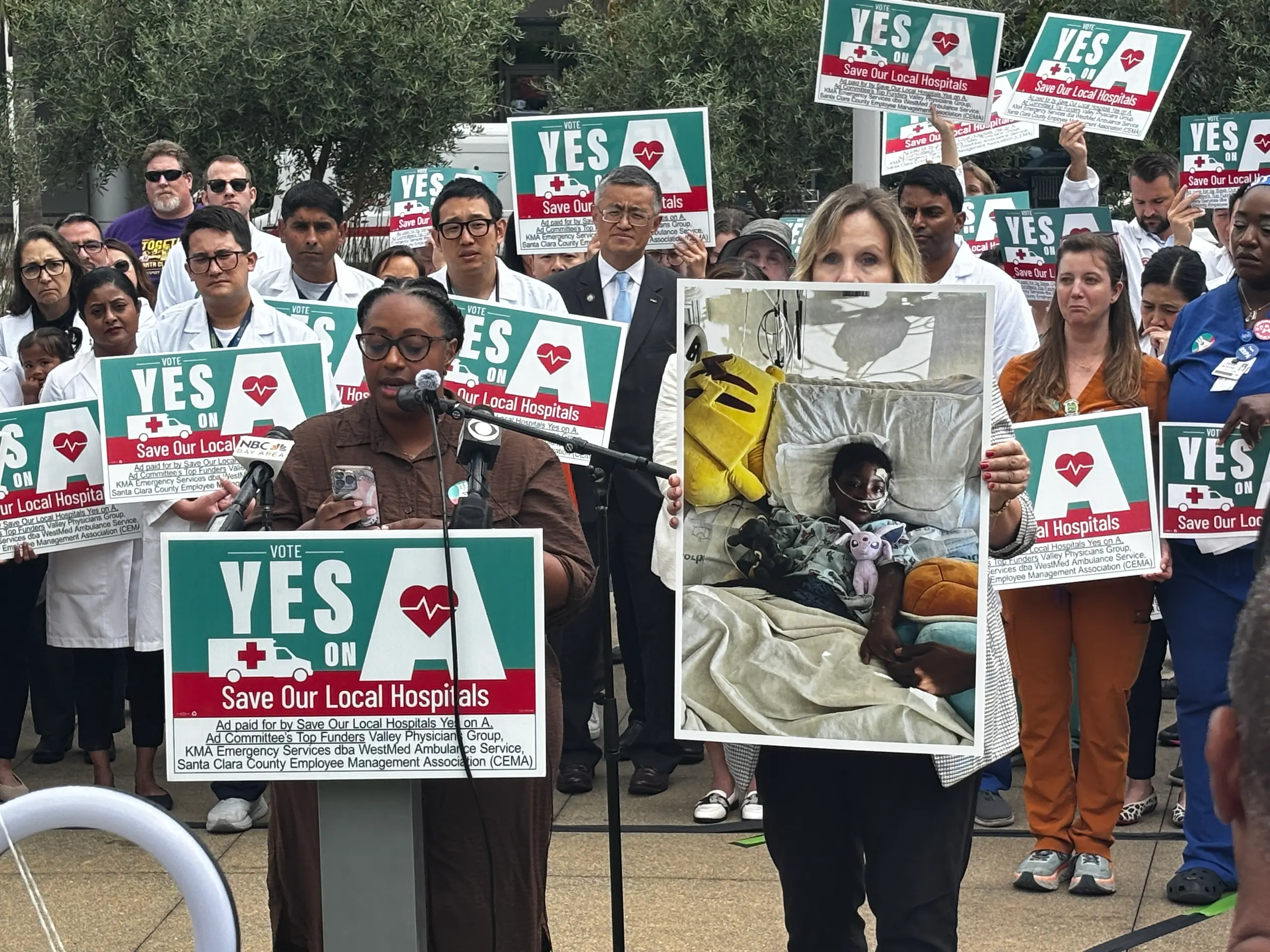 Habla Ashley Mompoint-Michel mientras una amiga sostiene la foto del hijo de Ashley. Dice que los médicos de Valley Medical salvaron la vida de su hijo. La familia vive en San José. 