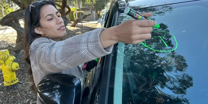 Elida Valencia Sobalvarro se estira para escribir una T de pavo en el parabrisas de un conductor durante una distribución de alimentos navideños de la YMCA en el sur de San Francisco, donde la financiación del condado garantizó que cientos de familias pudieran llevarse a casa una comida navideña.